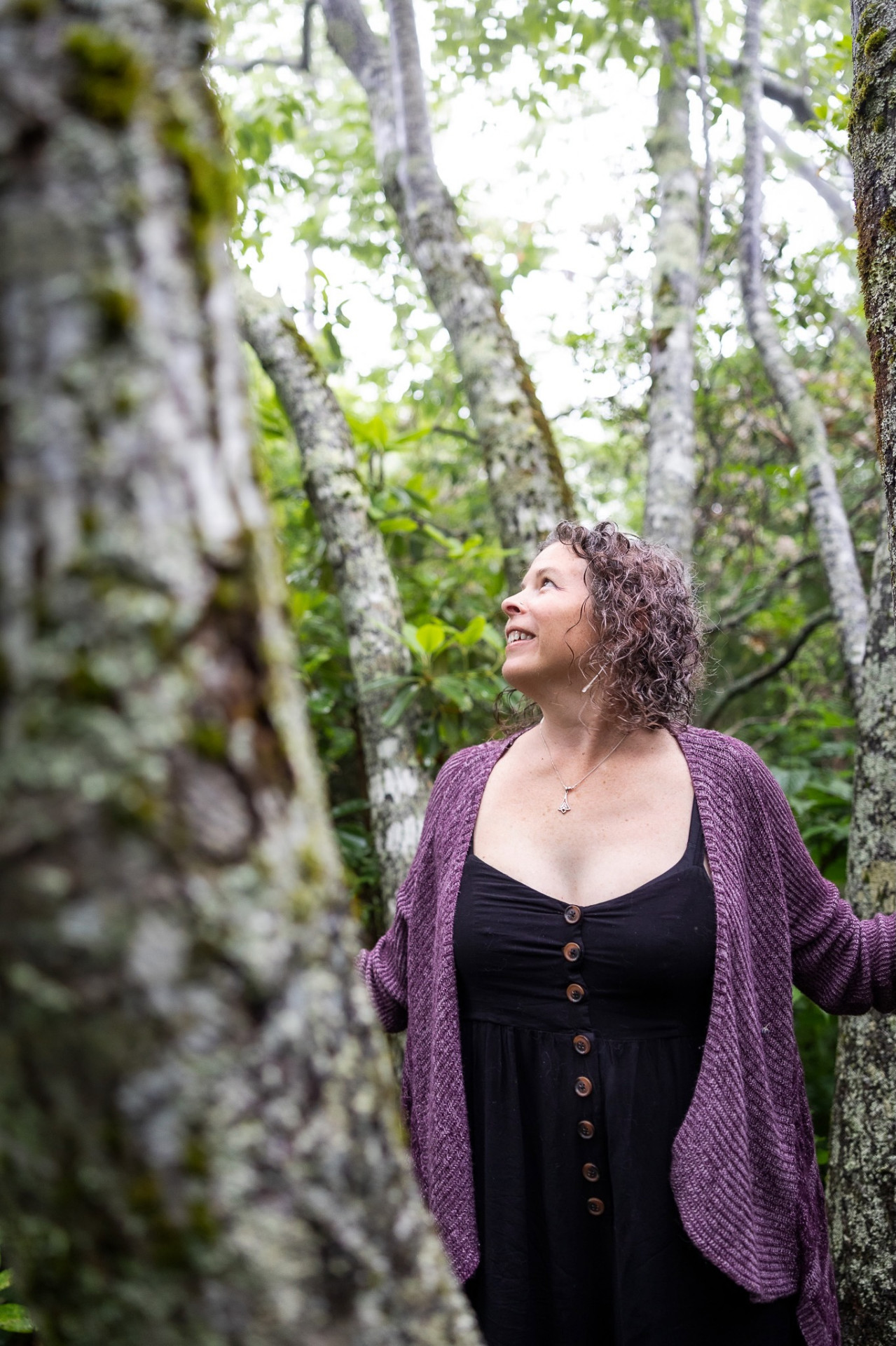 Bre standing among mossy trees, looking up.