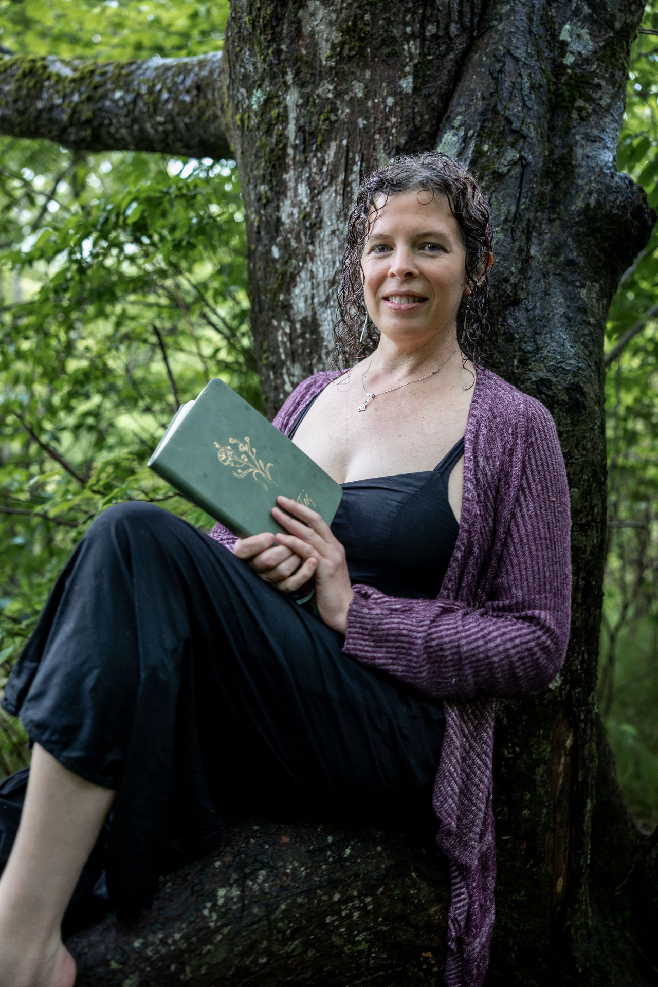 Rachel seated against a mossy tree, holding a green journal